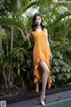 A woman in an orange dress standing next to a pool.