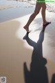 A woman walking on a beach with her shadow on the sand.