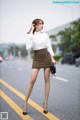 A woman in a white shirt and brown skirt is walking down the street.