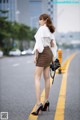 A woman in a white blouse and brown skirt is standing on the street.