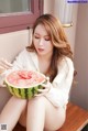 A woman sitting on a bench eating a watermelon.