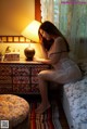 A woman sitting on a bed next to a lamp.