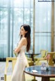 A woman in a white dress standing next to a table.