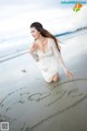 A woman in a white dress writing in the sand on the beach.