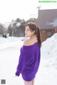 A woman in a purple sweater is standing in the snow.