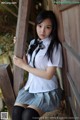 A woman in a school uniform leaning against a wooden fence.