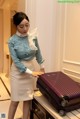 A woman in a blue shirt and white skirt holding a purple suitcase.