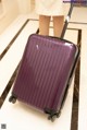 A woman standing next to a purple suitcase on a marble floor.