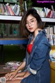 A woman sitting on a bench in front of a bookshelf.