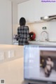 A woman standing in a kitchen looking at a television.