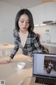 A woman sitting at a kitchen counter looking at a laptop computer.