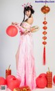 A woman in a pink dress holding a fan and red lanterns.