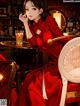 A woman in a red dress sitting at a table with a glass of wine.