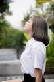 A woman in a white shirt and black skirt sitting on a bench.