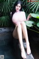 A woman in a pink bodysuit sitting on a ledge next to a pool.