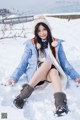 A woman sitting in the snow wearing a blue jacket and boots.