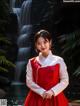 A woman in a red and white dress standing in front of a waterfall.