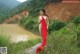 A naked woman in a red dress standing by a river.