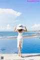 A woman in a white dress and hat standing by a swimming pool.