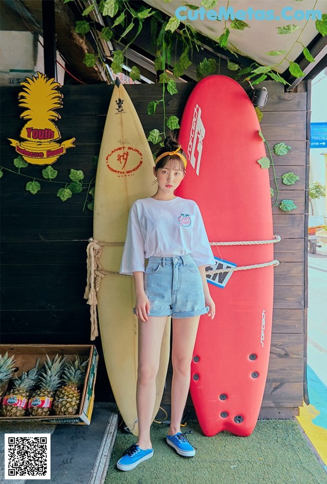 A woman standing next to a red surfboard in front of a building.