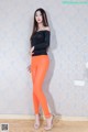 A woman in a black top and orange leggings posing for a picture.