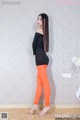 A woman in a black top and orange leggings posing for a picture.