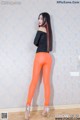 A woman in a black top and orange leggings posing for a picture.