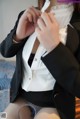 A woman in a black suit and white shirt is putting on her panties.