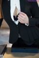 A woman in a black suit is putting on a white shirt.