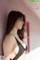 A woman in a black bra leaning against a pink wall.