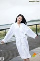 A woman in a white bathrobe standing on a boardwalk.